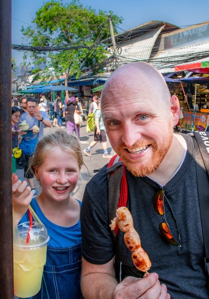 Chris eating a kabob and Lucy with a drink in a bag from the day market 