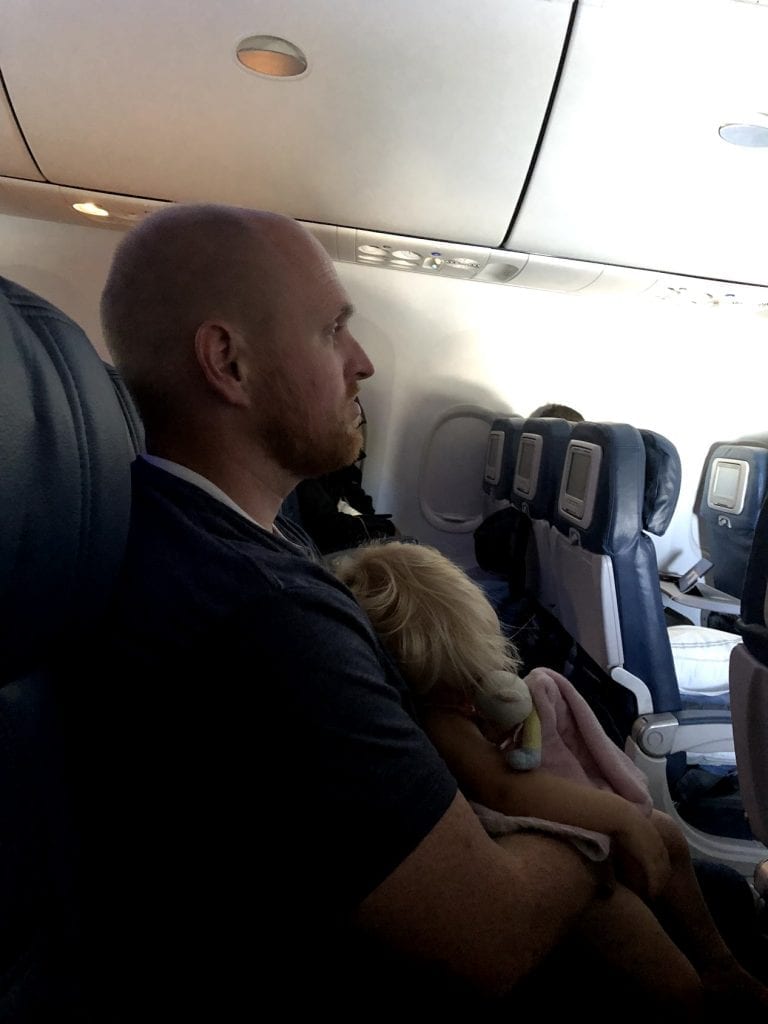 The baby asleep on the airplane while Chris holds her