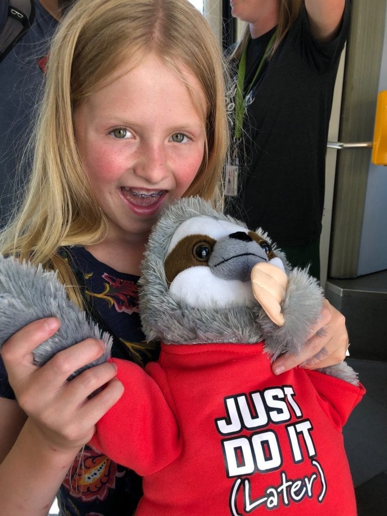 Lucy and a stuffed sloth wearing a shirt that says "Just Do It (later)"