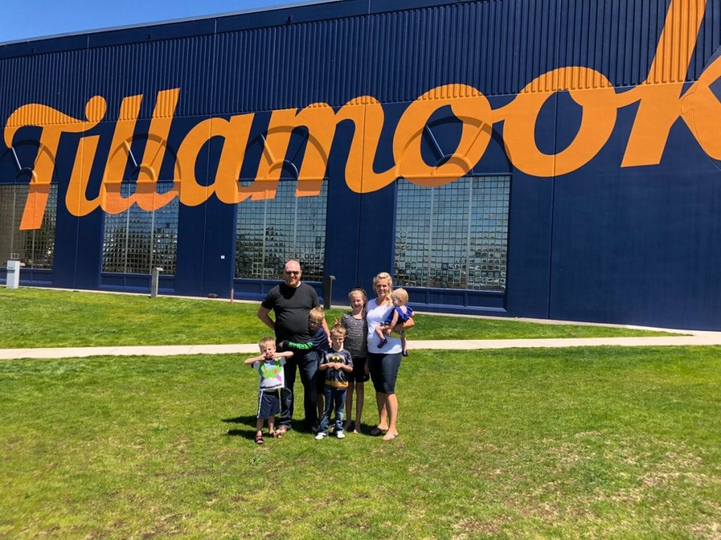 Family picture outside of the Tillamook factory- a blue building with "Tillamook" written in yellow cursive letters.