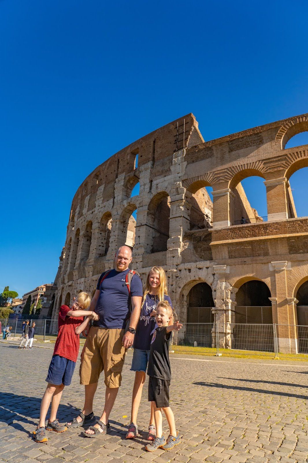 Two adults and several children pose in front of the Colosseum.