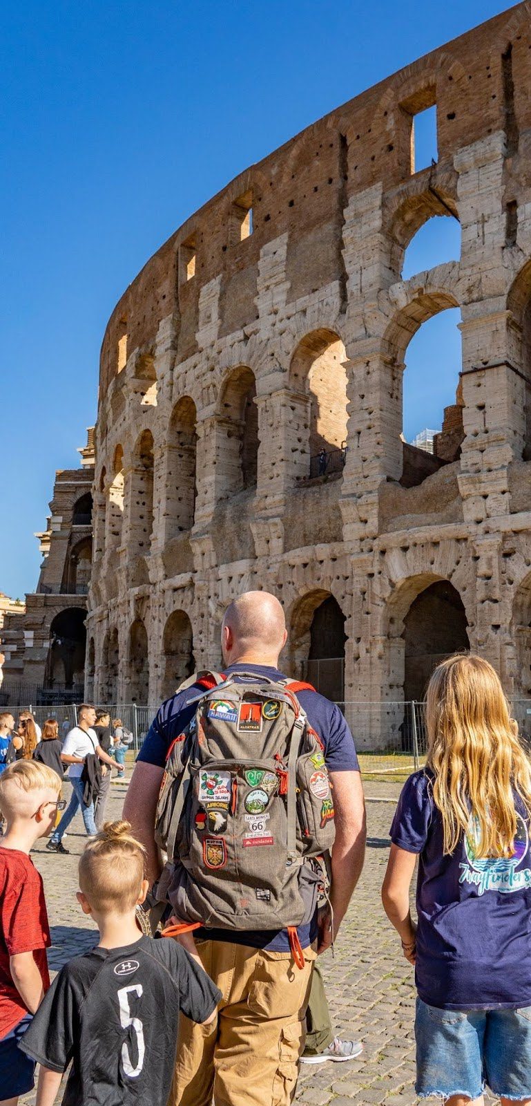 A family stands outside the Colosseum, viewed from behind.