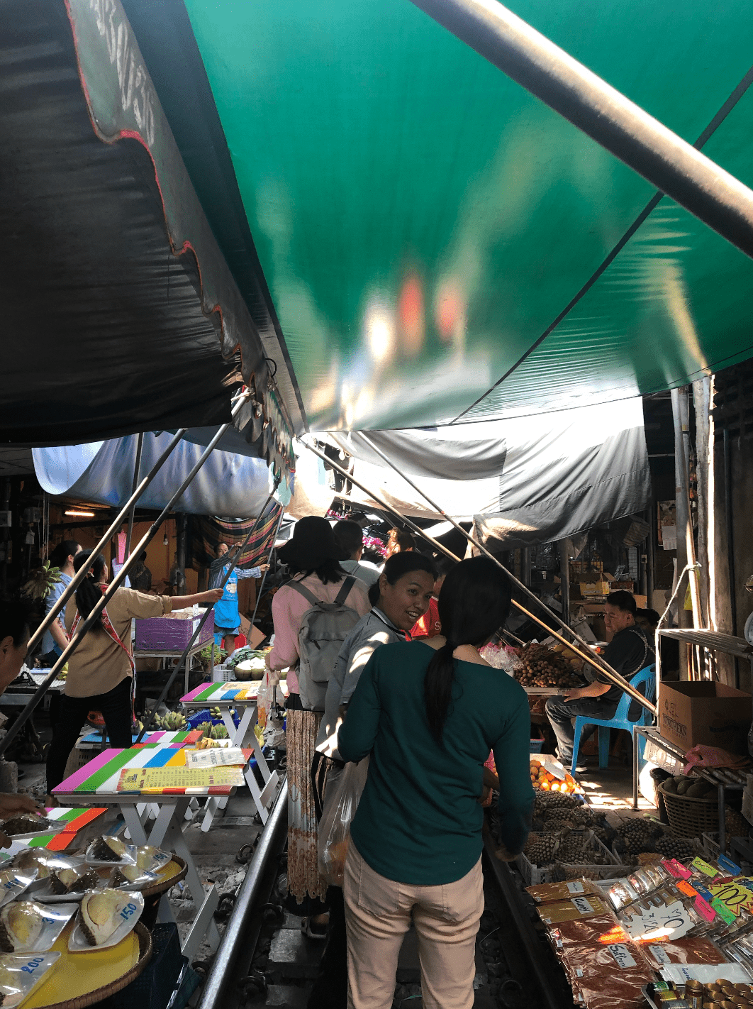 Shoppers browse stalls beneath the covered Maeklong market roof beside the railway tracks.