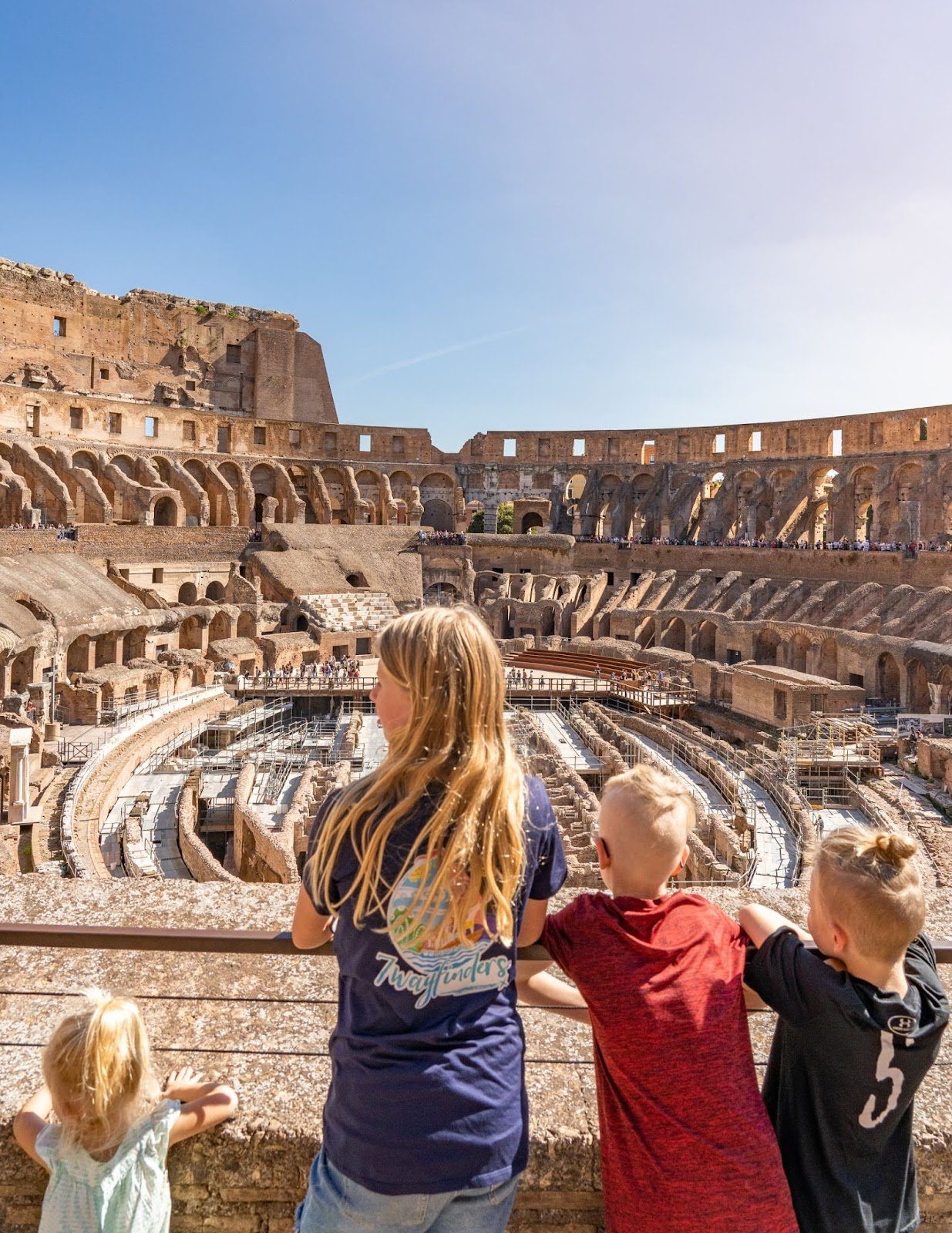 Children and adults look into the Colosseum arena from a viewing rail.