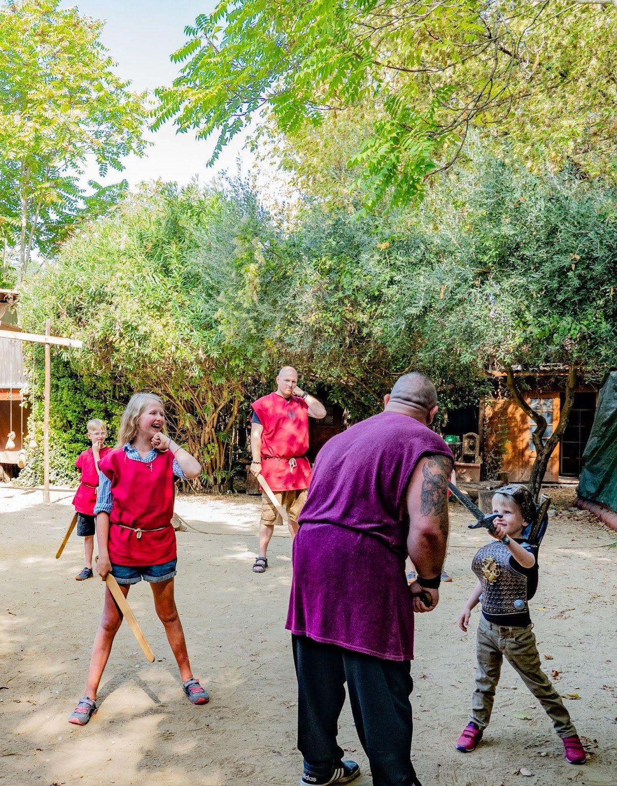 A costumed reenactor and a child in Roman-style tunics practice with wooden swords in a courtyard.