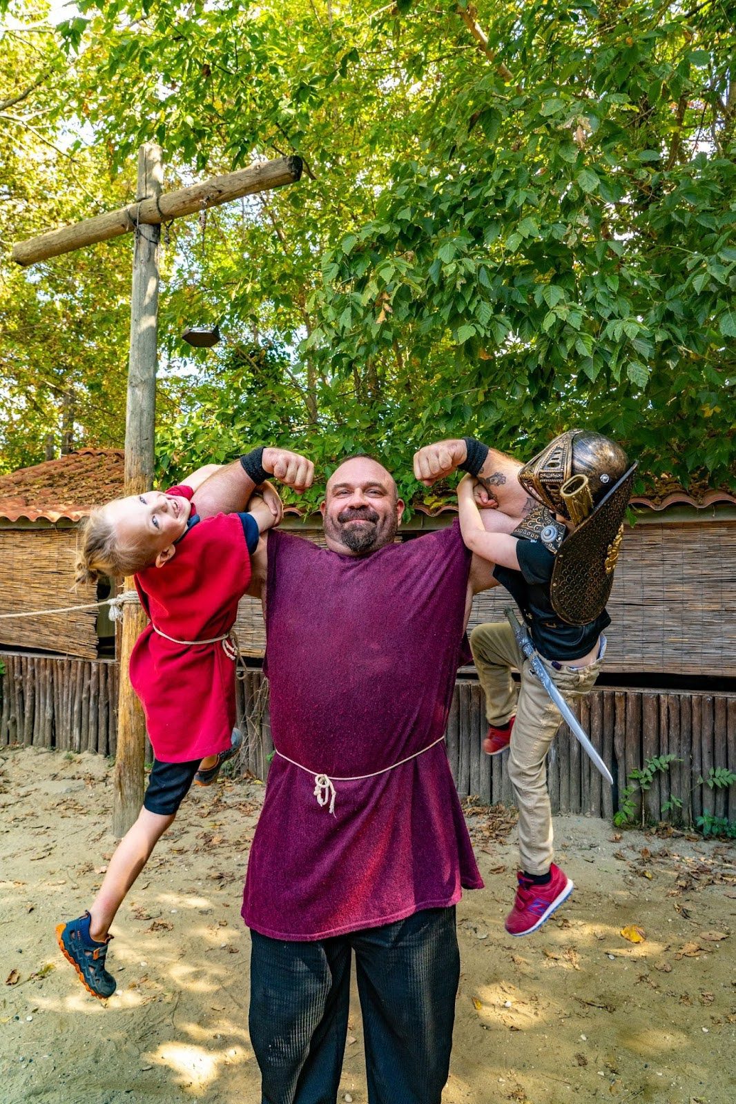 A costumed reenactor and two children in tunics pose with flexed arms.