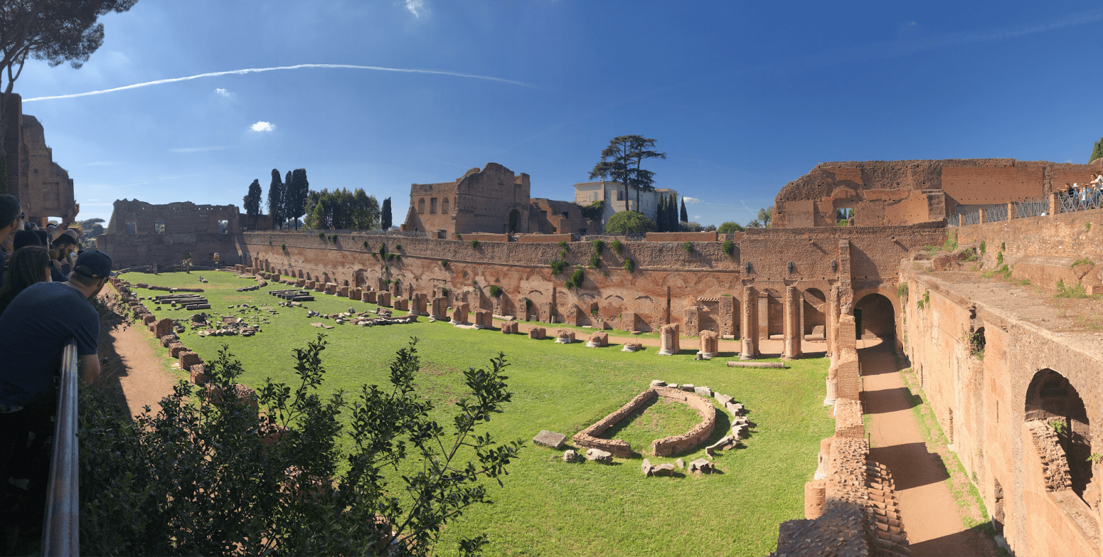 Visitors walk beside a long brick-and-stone ruin in an archaeological area in Rome.