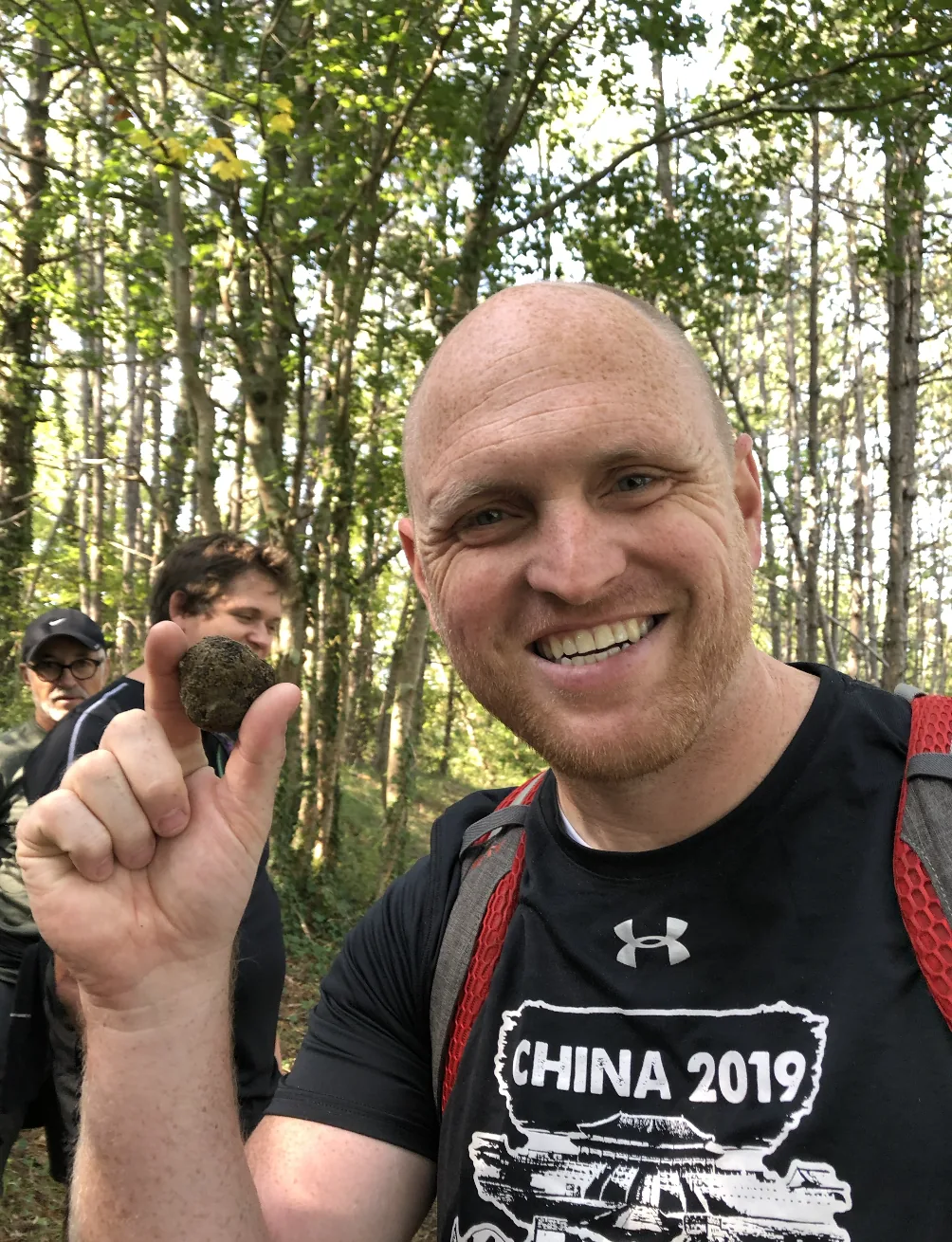 A man smiles while holding a truffle in the forest.