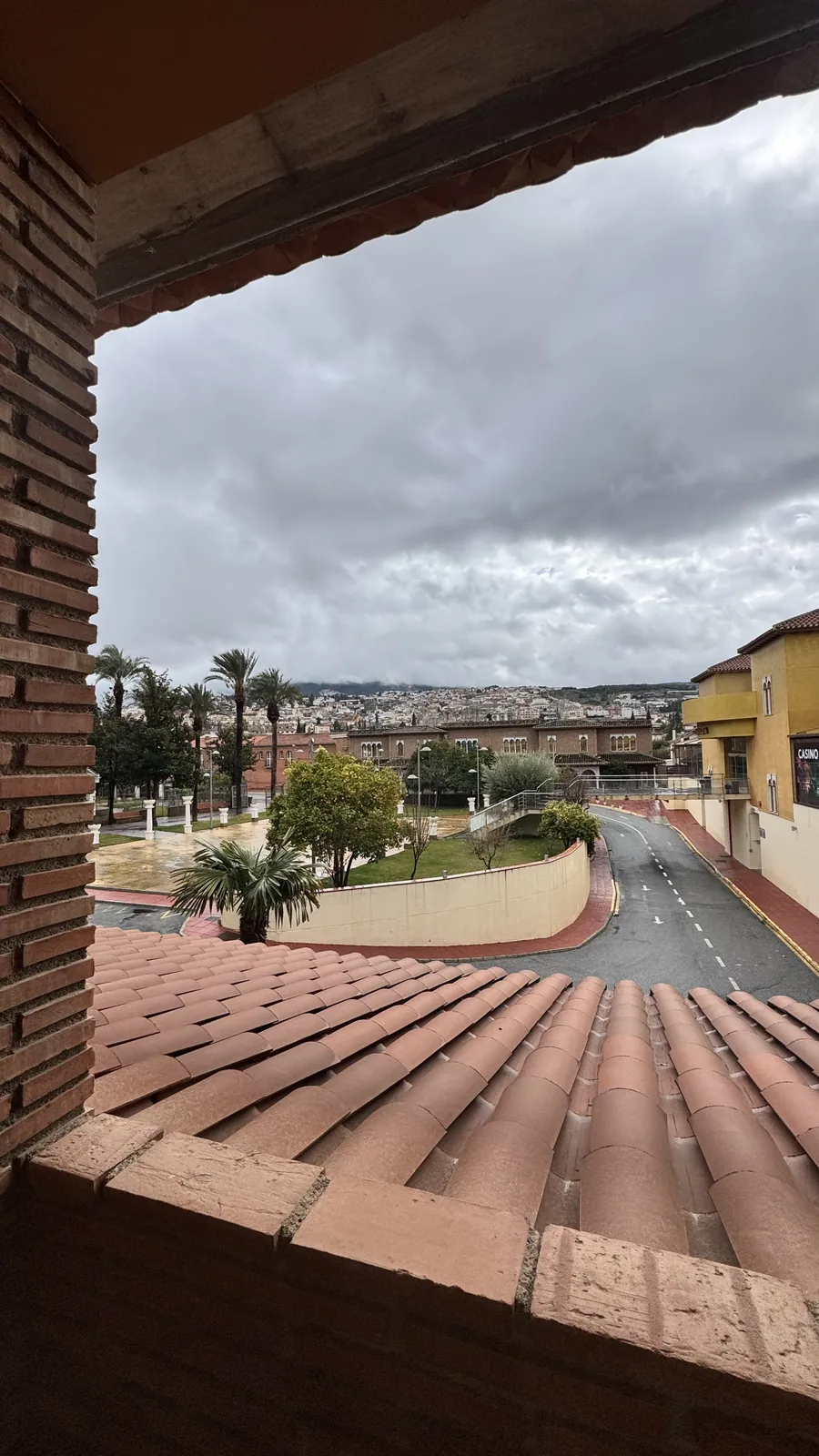 View over Granada rooftops and a courtyard from a covered terrace.