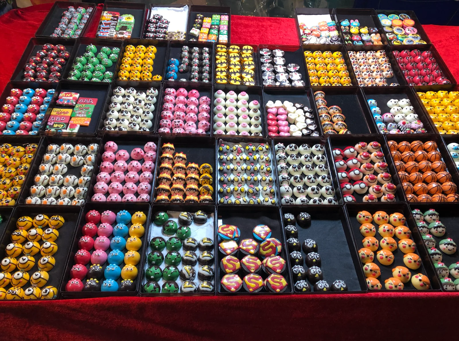 Rows of small colorful molded chocolates are displayed in trays.