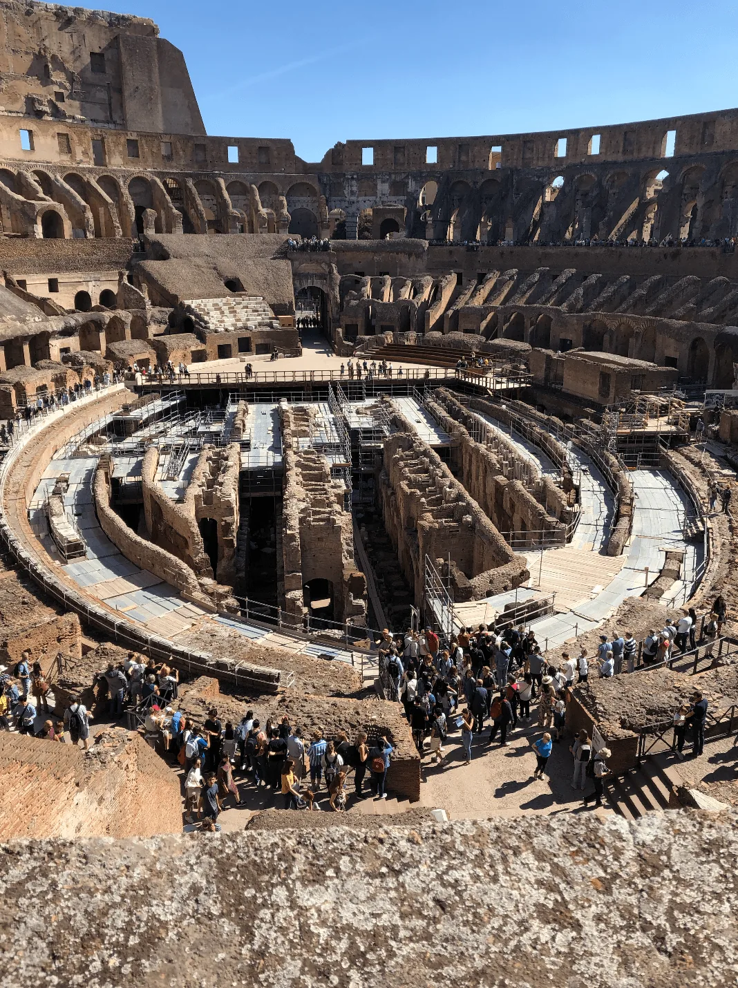 Visitors look down over the Colosseum arena and its exposed underground structures.